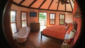 A bedroom with a large bed, a bathtub, and a wooden floor.