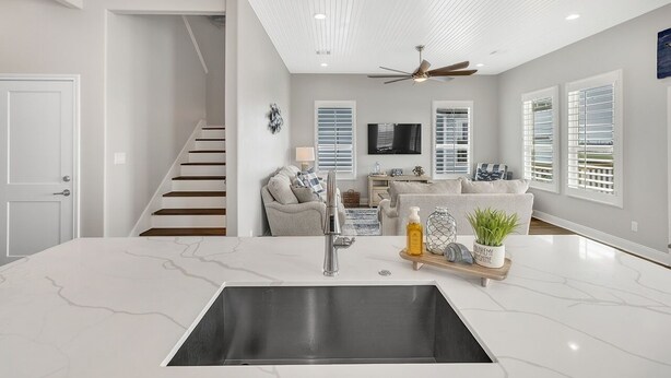 A modern kitchen with a marble countertop, stainless steel sink, and a ceiling fan. - Fishermans Delight 3 Bedroom Home by RedAwning (Port Bolivar)