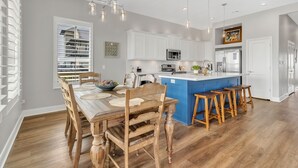 A modern kitchen with white cabinets, a blue island, and wooden bar stools. - Fishermans Delight 3 Bedroom Home by RedAwning (Port Bolivar)
