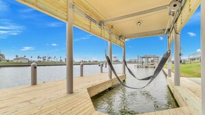 A wooden dock extending over water with a hammock hanging from the ceiling. - Fishermans Delight 3 Bedroom Home by RedAwning (Port Bolivar)