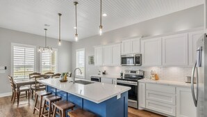 A modern kitchen with white cabinetry, a blue island, wooden stools, and pendant lighting. - Fishermans Delight 3 Bedroom Home by RedAwning (Port Bolivar)