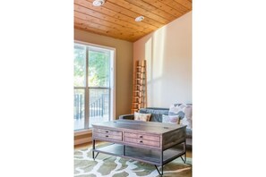 Relax in this spacious room with a high ceiling, featuring a large window offering a view of lush greenery outside.