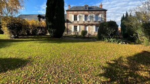 Una casa a due piani con un prato ampio e un albero alto in primo piano.