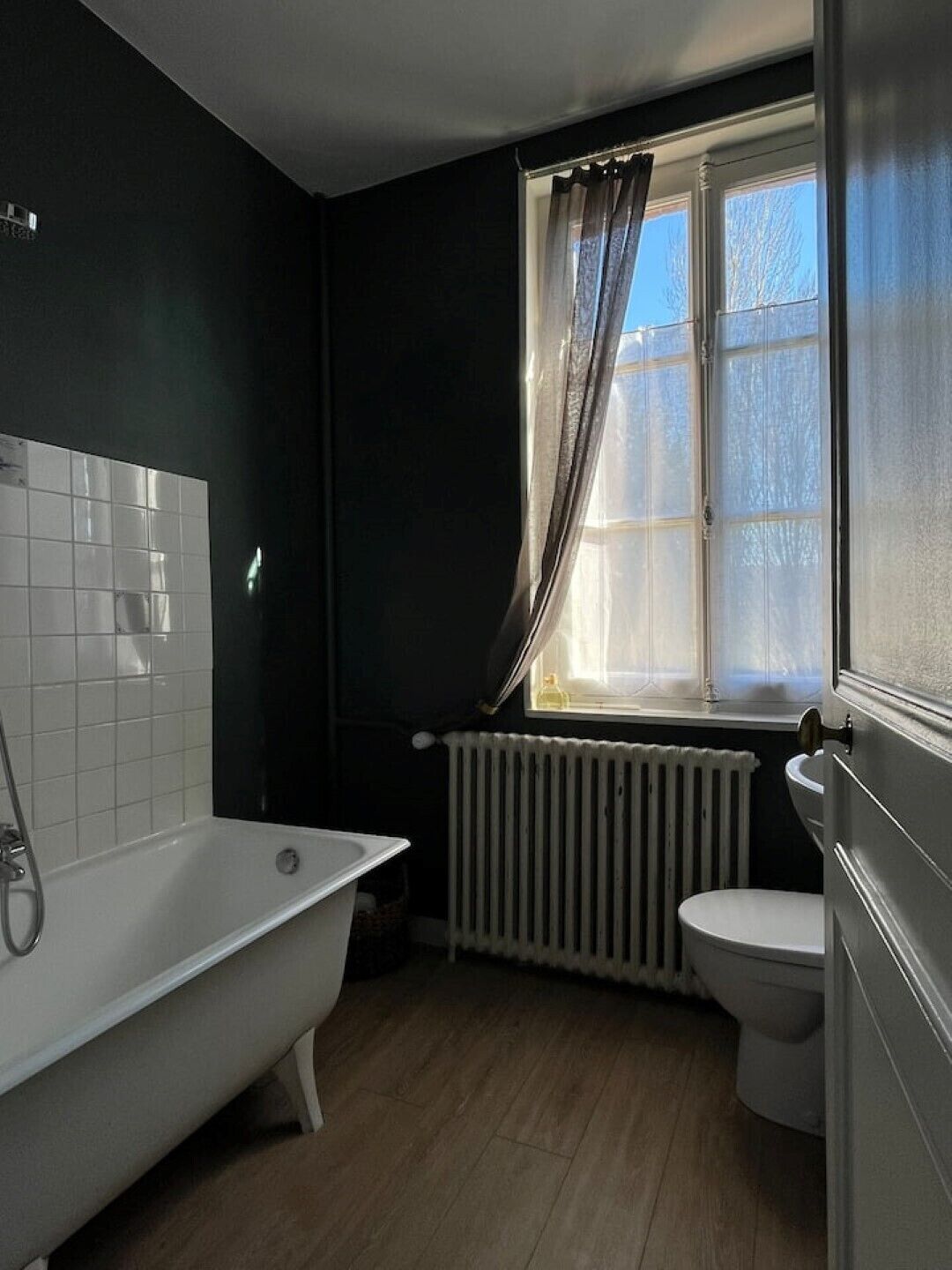 A bathroom with a bathtub, toilet, and a window with curtains.