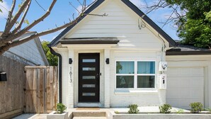 Une maison blanche d’un seul étage, avec une porte d’entrée noire, une petite fenêtre et une porte de garage.