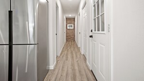Un couloir avec un réfrigérateur en acier inoxydable, des portes blanches et un plancher en bois.