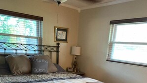Un dormitorio con cama, suelo de madera, mesita de noche, lámpara y ventana.