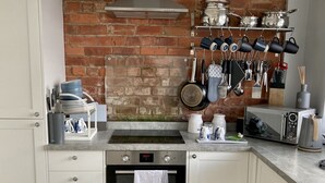 A kitchen with white cabinets, a brick wall, a stainless steel range hood, a microwave, and various kitchen utensils.