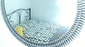 A circular mirror with a decorative frame, a bed with patterned bedding, a black metal headboard, and a green pendant light.