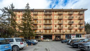 A multi-story building with a row of balconies on each floor, a parking lot in front, and a sign indicating a promotional sale.
