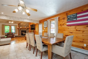A wooden interior with a dining table, chairs, a fireplace, and a ceiling fan.