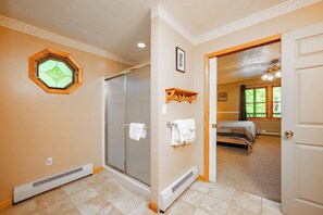 A bathroom with a shower, a towel rack, and a small window with a decorative frame.