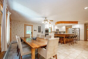 Une cuisine spacieuse avec un îlot central en bois, un coin repas avec une grande table et des chaises, et un ventilateur de plafond.