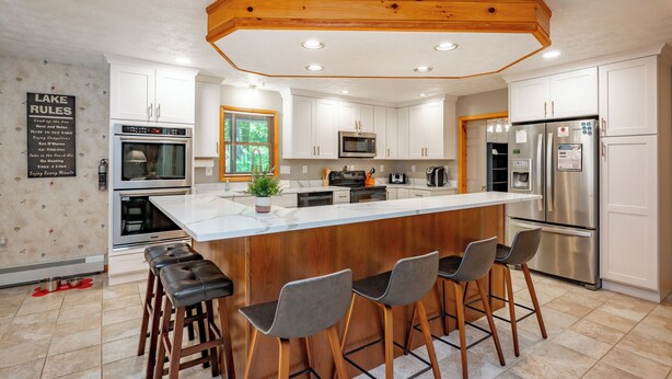 Een moderne keuken met witte kasten, roestvrijstalen apparatuur en een houten kookeiland met barstoelen.