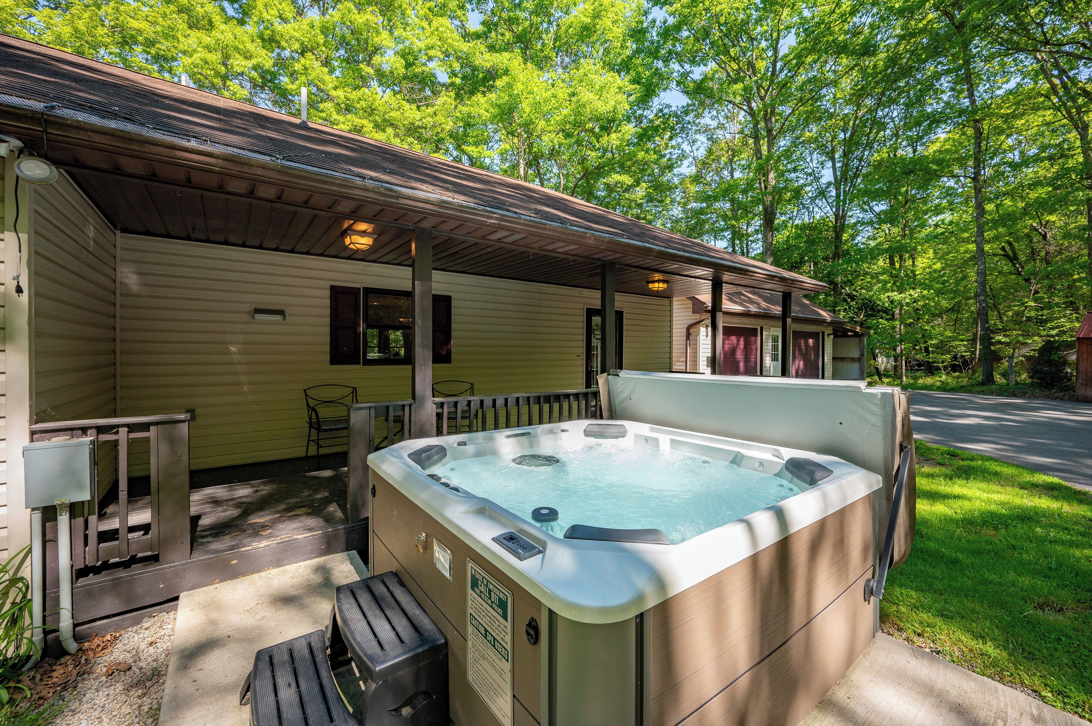 A hot tub outside a wooden cabin with a covered porch, a bench, and a trash can.