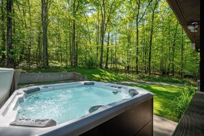 Un bain à remous situé dans une zone boisée, offrant une vue sur de grands arbres et un ciel dégagé.