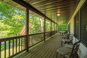 A covered porch with wooden railings, outdoor furniture, and a view of a green landscape.