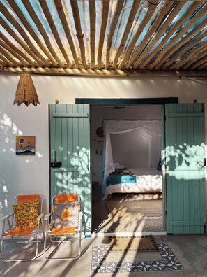 An open doorway leading to a bedroom with a bed, a chair, and a hanging lamp. - Pousada Céu de Corumbau (Prado)