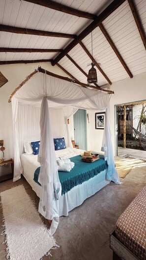 A bedroom with a canopy bed, a hanging light fixture, and a view of the outdoors. - Pousada Céu de Corumbau (Prado)