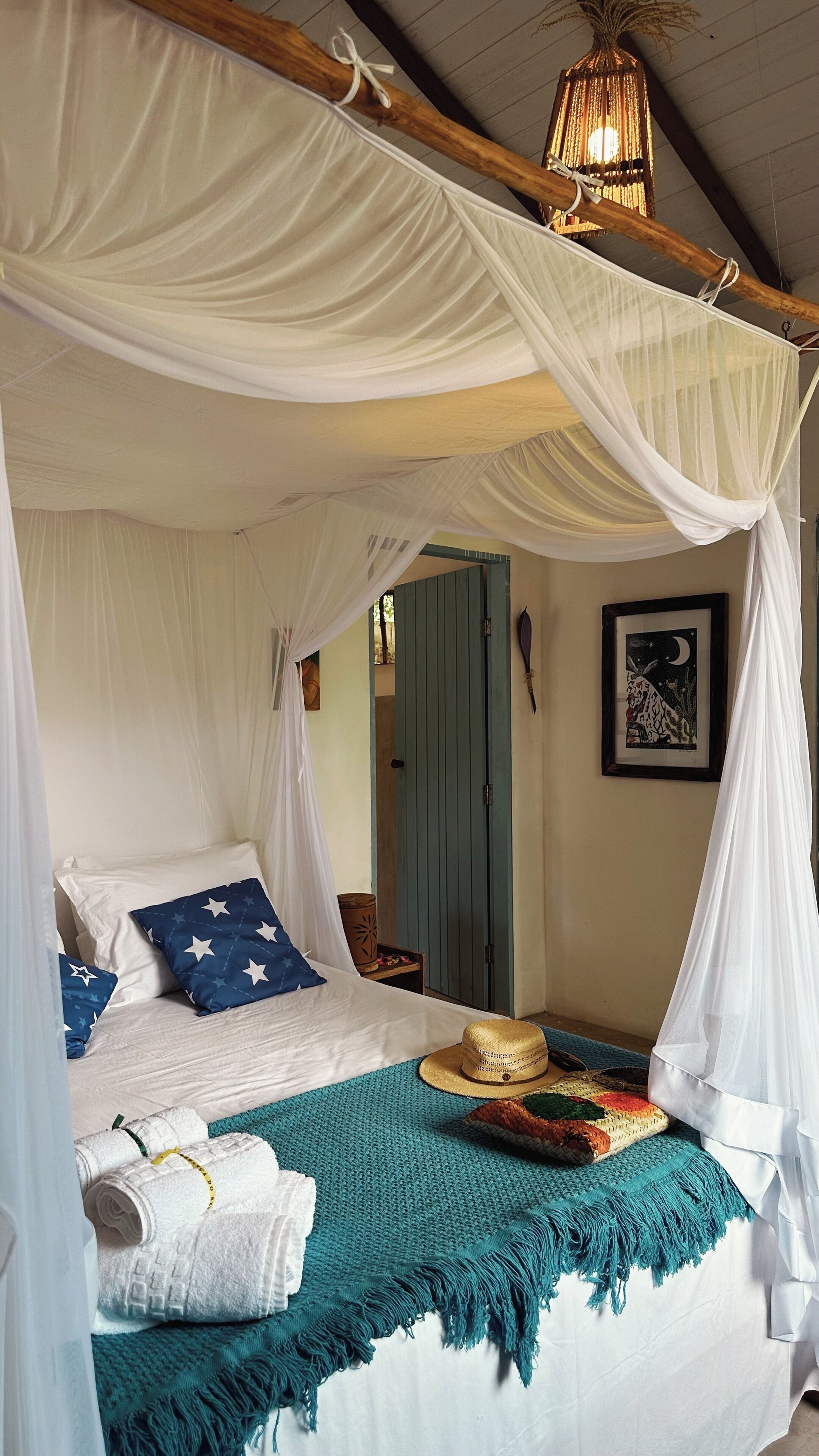 Una cama con dosel, almohada azul con motivos de estrellas, sombrero de paja y manta tejida.