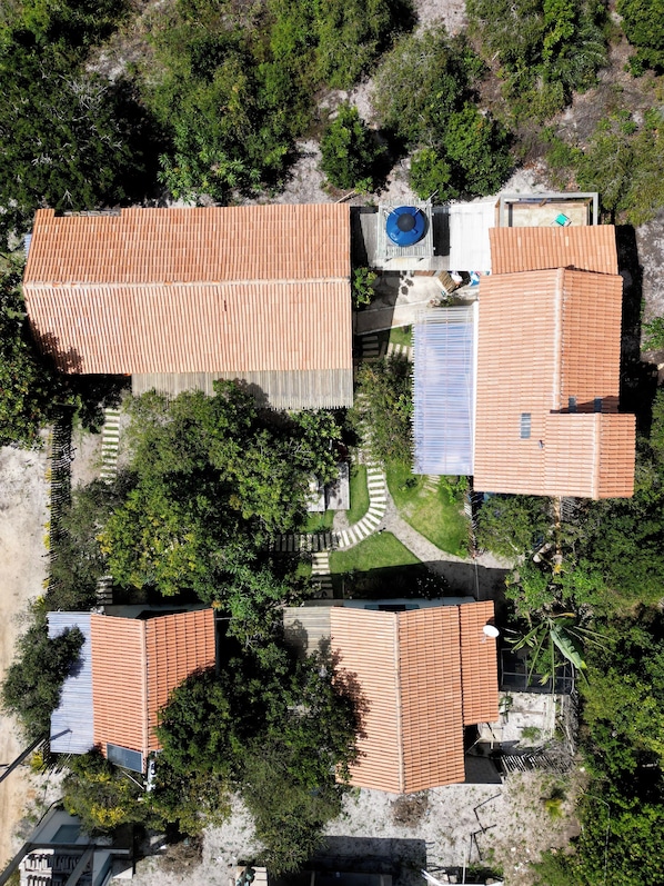 An aerial view of a residential area with multiple houses featuring red-tiled roofs, surrounded by greenery and a clear sky. - Pousada Céu de Corumbau (Prado)