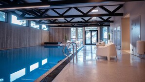A modern indoor swimming pool with a clear view of the sky through large windows, a metal pool ladder, and a seating area with white chairs. - Awesome apartment in Søgne with sauna (Søgne)