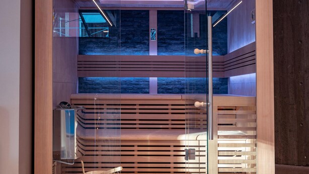 A sauna with a wooden interior, glass walls, and a stone wall backdrop. - Awesome apartment in Søgne with sauna (Søgne)