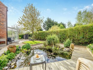 A garden with a pond, seating area, and a glass-enclosed patio. - 1 bedroom accommodation in Stickford, near Spilsby (Stickford, near Spilsby)