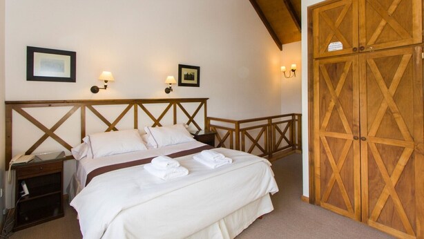 Un dormitorio con cabecera de madera, cama con ropa de cama blanca, dos lámparas de noche y un armario de madera.