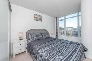 Relax in this serene bedroom with a large bed, tufted headboard, and city views.
