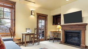 Un salón acogedor con chimenea, un televisor montado encima y una ventana con vistas a árboles.