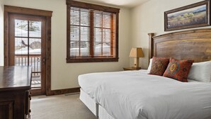 Un dormitorio con una cama grande, un cabecero de madera, una mesita de noche con una lámpara y una ventana con persianas.