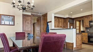 A dining area with a glass table and four upholstered chairs, wooden cabinets, and a kitchen in the background. - Outpost: Grand View 5020A - Fireplace, Elevator, AC! (Jackson)