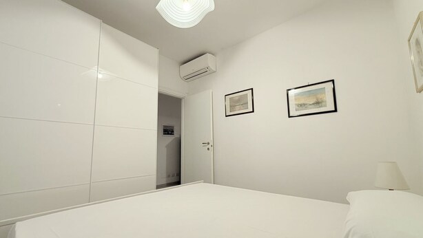 A bedroom with a bed, white walls, two framed pictures, an air conditioning unit, and a door leading to another room. - M333 - Marcelli, cozy two-room apartment 200 meters from the beach (Marcelli)
