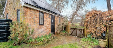 Une maison en briques avec un toit en pente, un portail en bois et un jardin avec de la pelouse et des plantes.