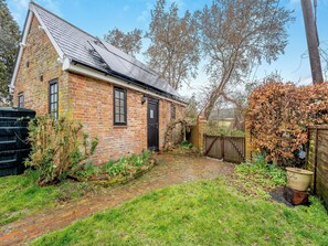 A brick house with a sloped roof, a wooden gate, and a garden with grass and plants. - 1 bedroom accommodation in Heathfield (Heathfield)