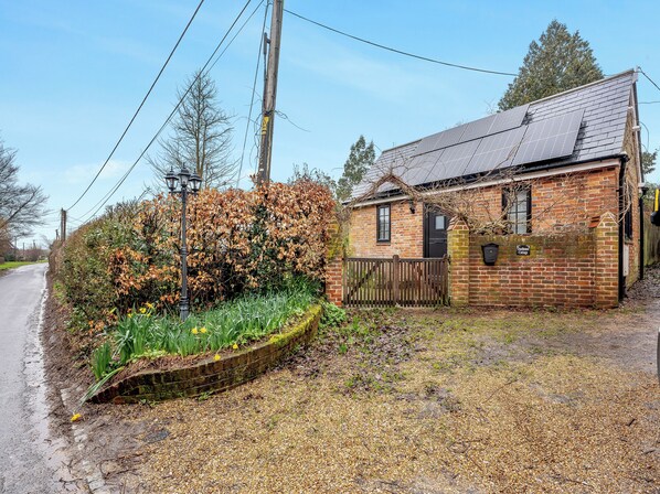 A brick cottage with a metal roof, a wooden fence, and a garden with daffodils. - 1 bedroom accommodation in Heathfield (Heathfield)