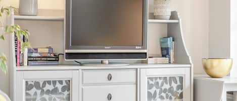 Un televisor sobre un mueble, una planta y libros.