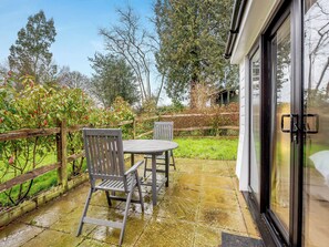 A patio with two wooden chairs and a table, a wooden fence, and a glass door leading to a covered area. - 1 bedroom accommodation in Heathfield (Heathfield)