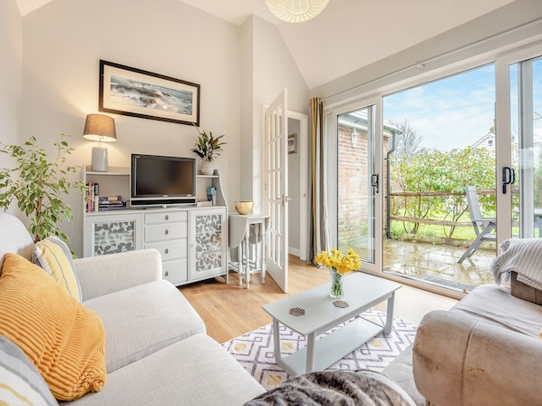 A modern living room with a sofa, coffee table, and a TV on a cabinet. - 1 bedroom accommodation in Heathfield (Heathfield)