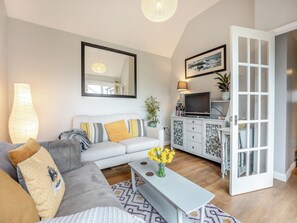 A modern living room with a sofa, coffee table, TV, and a cabinet with a glass door. - 1 bedroom accommodation in Heathfield (Heathfield)