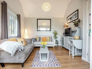 A living room with a grey sofa, a coffee table, a TV, and a dining area with a white cabinet. - 1 bedroom accommodation in Heathfield (Heathfield)