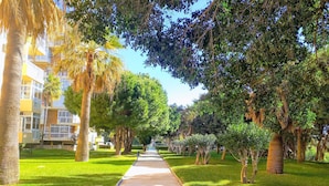A pathway lined with trees and grass, leading towards a building with balconies.