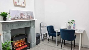 Un angolo accogliente con camino, un tavolino con sedie e uno scaffale a parete con oggetti decorativi.