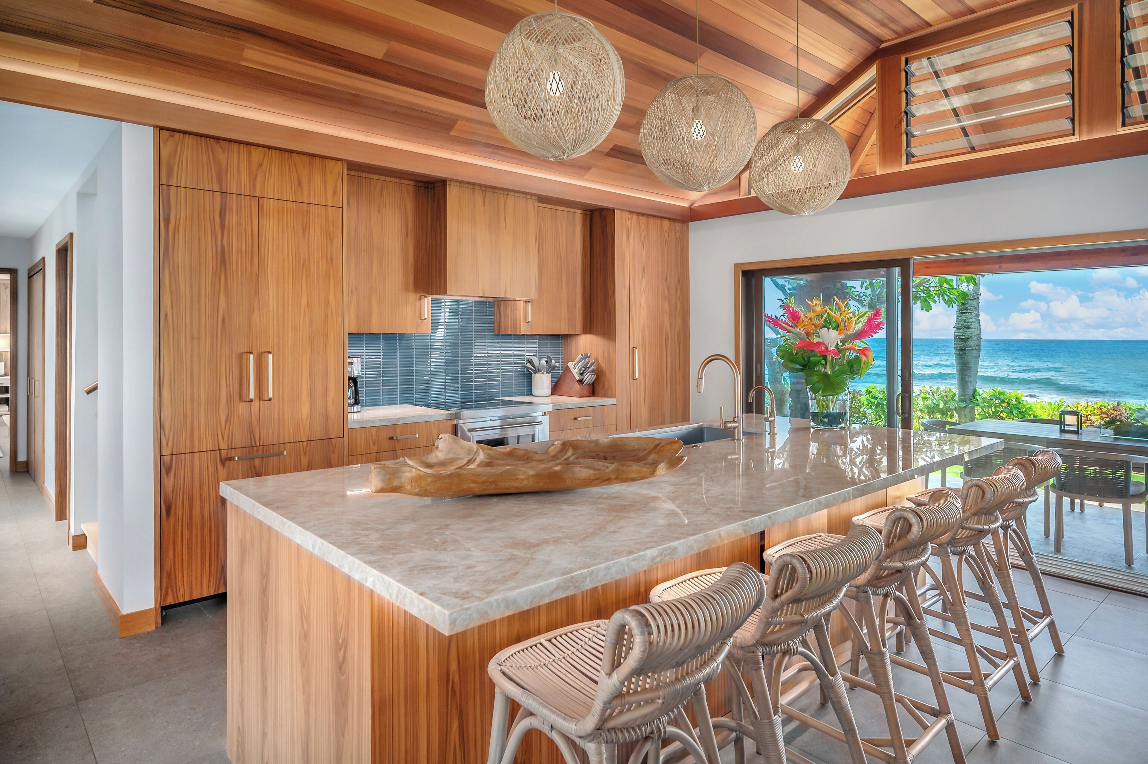 A modern kitchen with wooden cabinets, a large island with bar stools, and a view of the ocean.