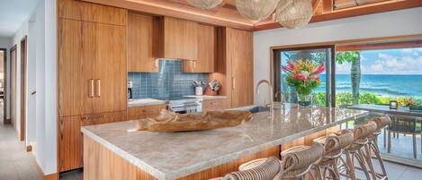 A modern kitchen with wooden cabinets, a large island with bar stools, and a view of the ocean.