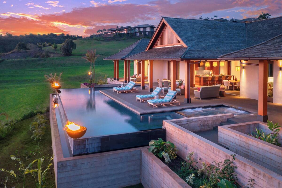 A modern outdoor pool area with lounge chairs and a hot tub, surrounded by wooden planters and a well-maintained lawn.
