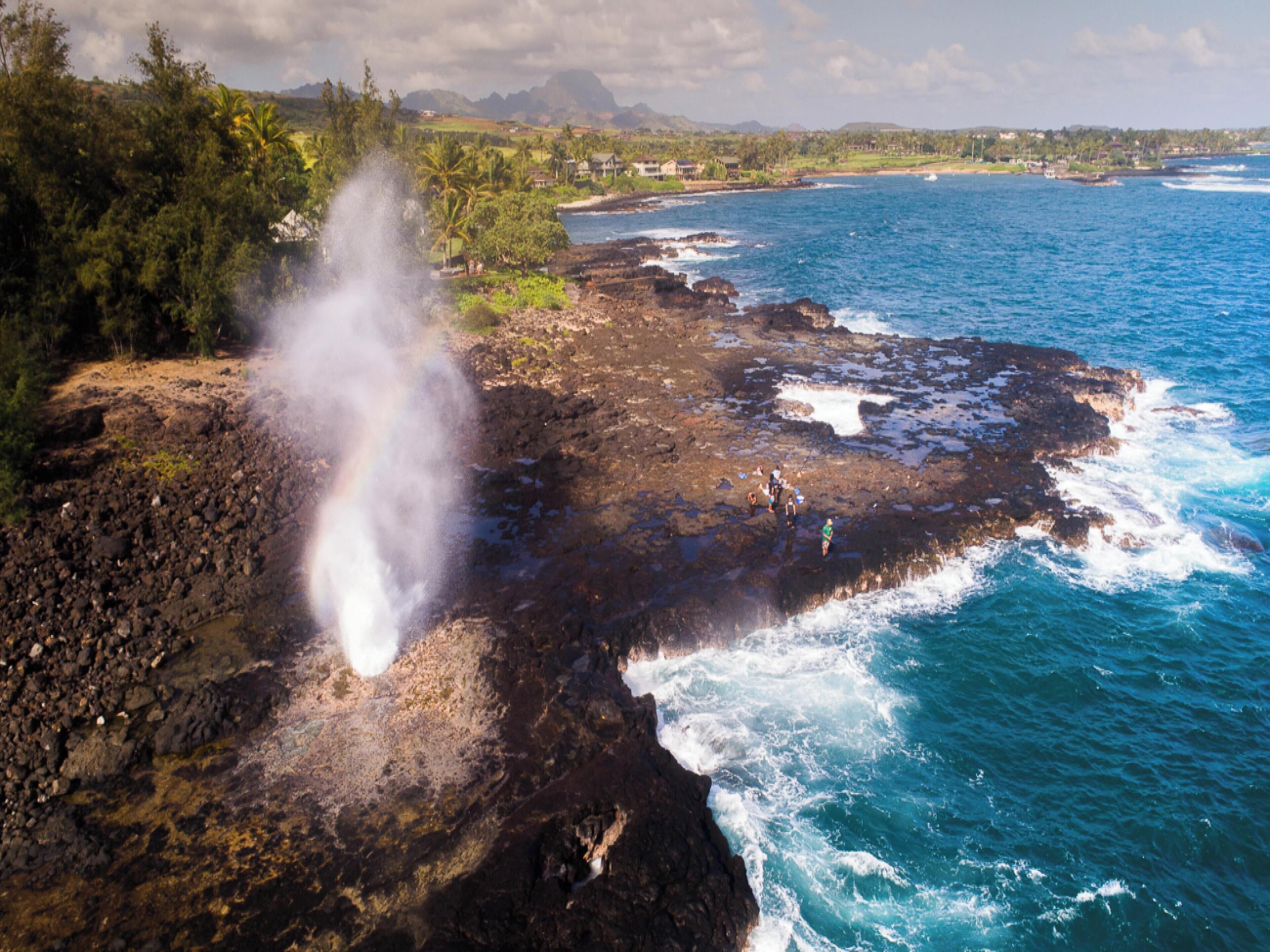 A coastal landscape with a rocky shoreline, ocean waves, and a visible steam vent.