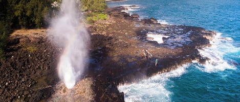 A coastal landscape with a rocky shoreline, ocean waves, and a visible steam vent.