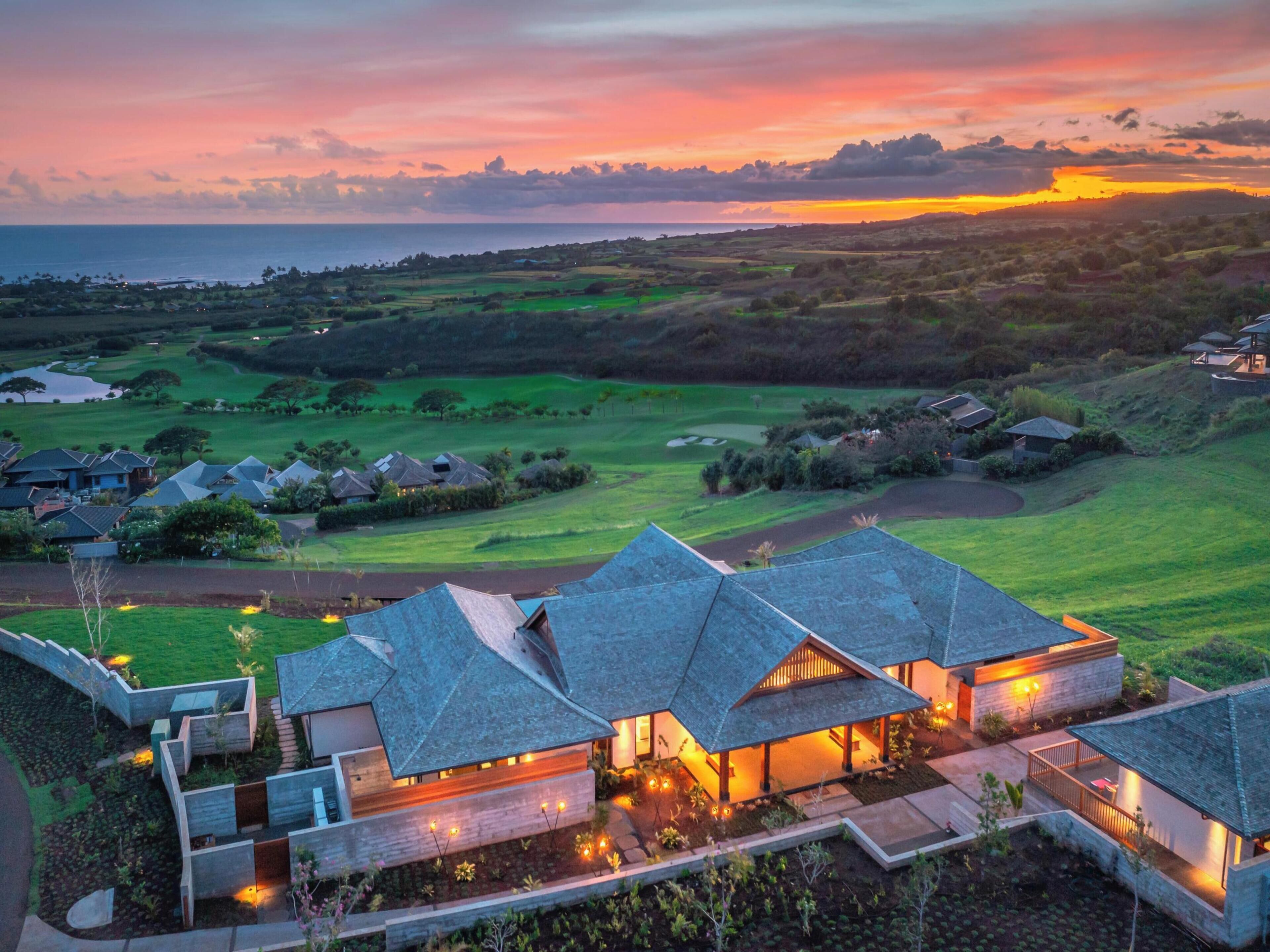 A modern resort with multiple buildings featuring sloped roofs, a well-maintained golf course, and a scenic ocean view.